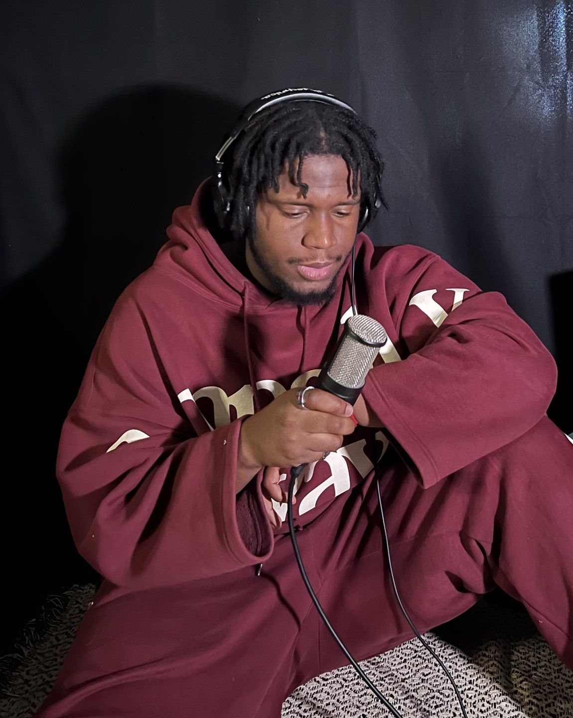 Yahya in a maroon Empathy Always hoodie with headphones, holding a studio mic